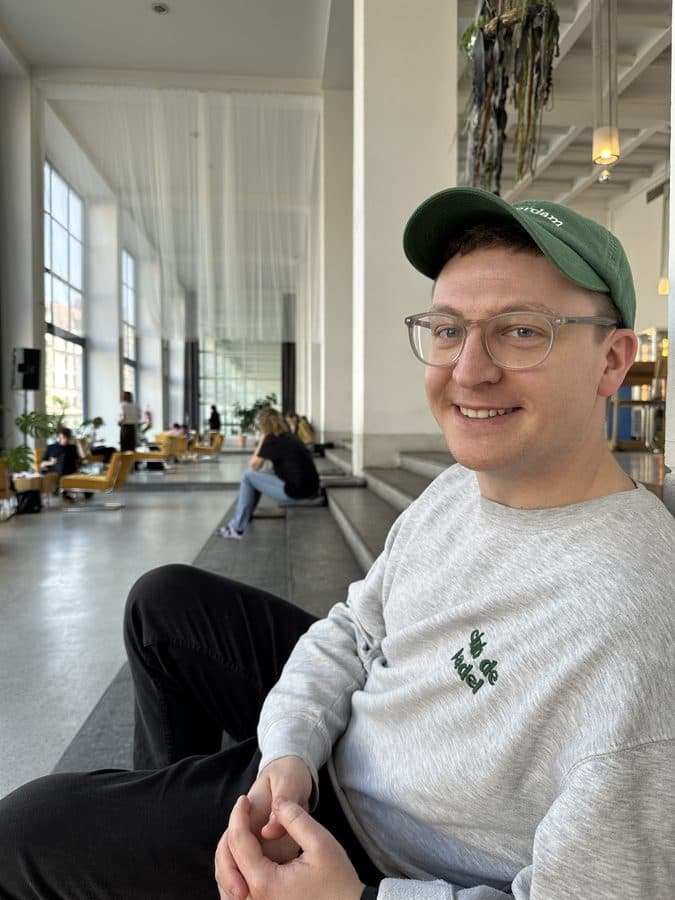 Aidan smiling in a bright, plant-filled lounge